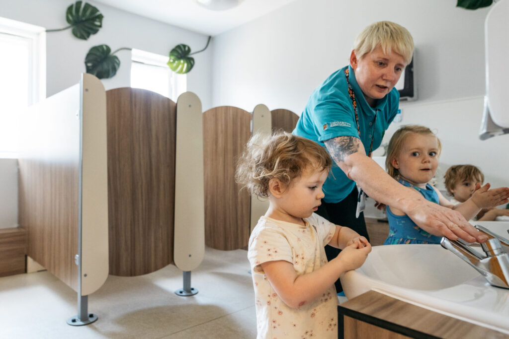 A member of staff helping children wash their hands.