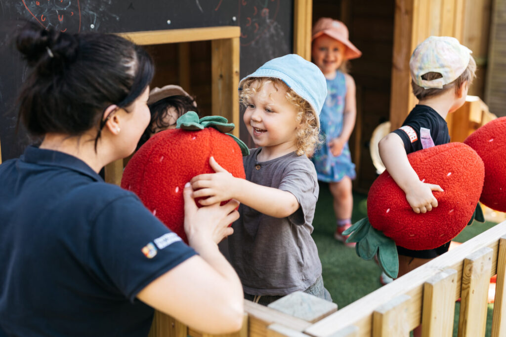 A child playing with a toy strawberry with a member of staff